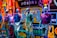 Mannequins displaying casual clothing are positioned inside a vibrant store window. The background is filled with colorful neon signs and lights, creating a bright and dynamic atmosphere. The mannequins are dressed in shorts and polo shirts, showcasing different styles and colors.