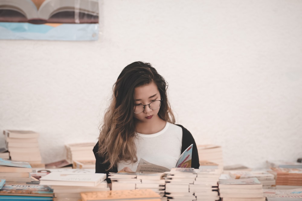 woman wearing white crew-neck shirt reading book surrounded with different books