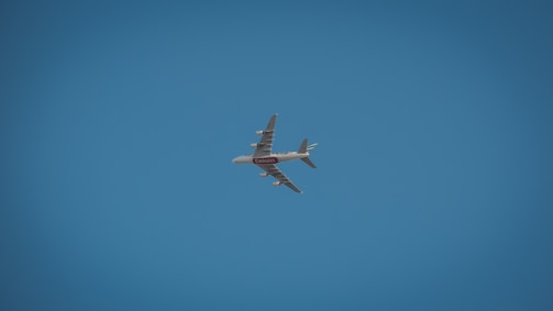 A large commercial airplane, possibly an Airbus, is flying against a clear blue sky. The aircraft is seen from below and is prominently marked with airline branding.