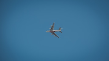A large commercial airplane, possibly an Airbus, is flying against a clear blue sky. The aircraft is seen from below and is prominently marked with airline branding.