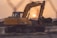 A heavy-duty excavator working on a rocky construction site during sunset.