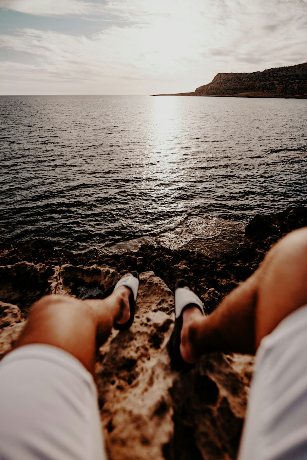 man wearing white shorts sitting on rock in front of water