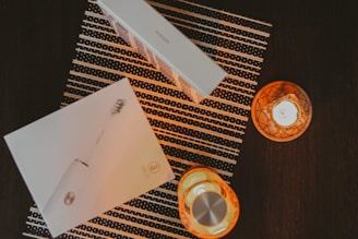 A flat lay composition featuring a boxed electric toothbrush placed on a striped mat. Two lit candles in orange holders create a warm, ambient glow on the dark surface.
