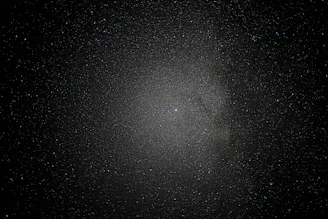 A vast expanse of space sprinkled with countless stars creates a mesmerizing view, with a dense cluster at the center suggesting a galaxy or nebula amid a dark, infinite void.