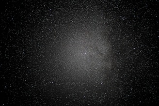 A vast expanse of space sprinkled with countless stars creates a mesmerizing view, with a dense cluster at the center suggesting a galaxy or nebula amid a dark, infinite void.