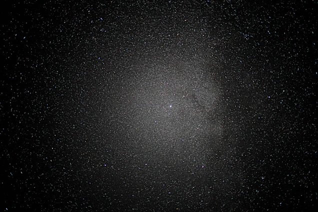 A vast expanse of space sprinkled with countless stars creates a mesmerizing view, with a dense cluster at the center suggesting a galaxy or nebula amid a dark, infinite void.