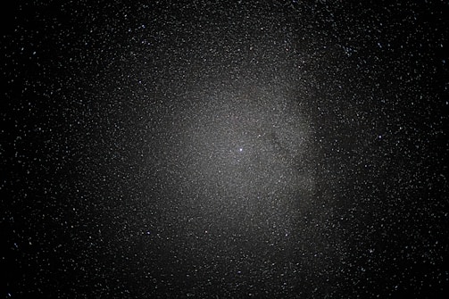 A vast expanse of space sprinkled with countless stars creates a mesmerizing view, with a dense cluster at the center suggesting a galaxy or nebula amid a dark, infinite void.