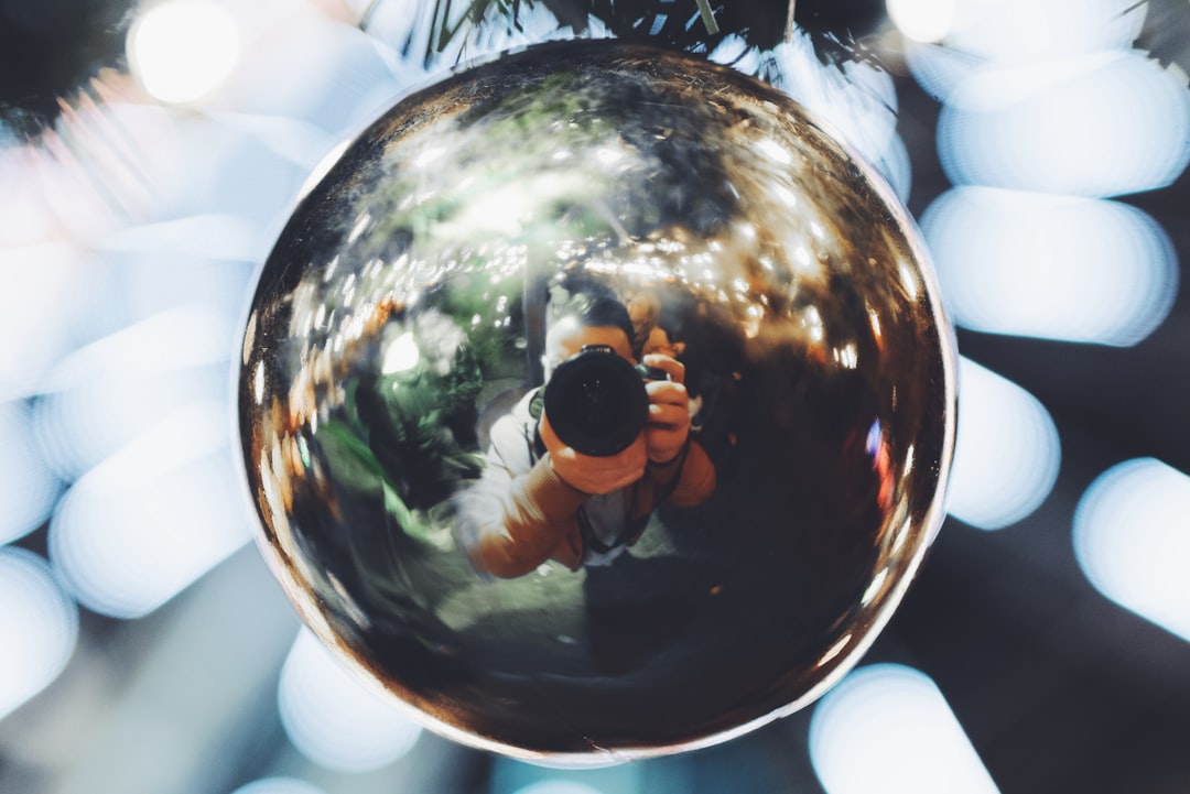 selective focus photography of bauble reflecting man holding camera