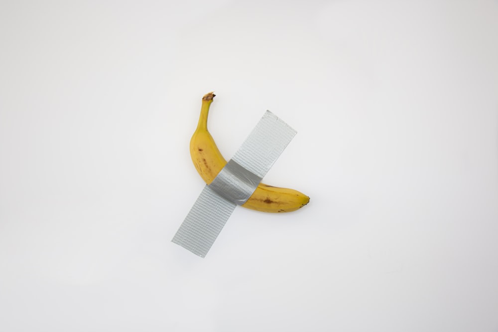 taped yellow banana on white surface