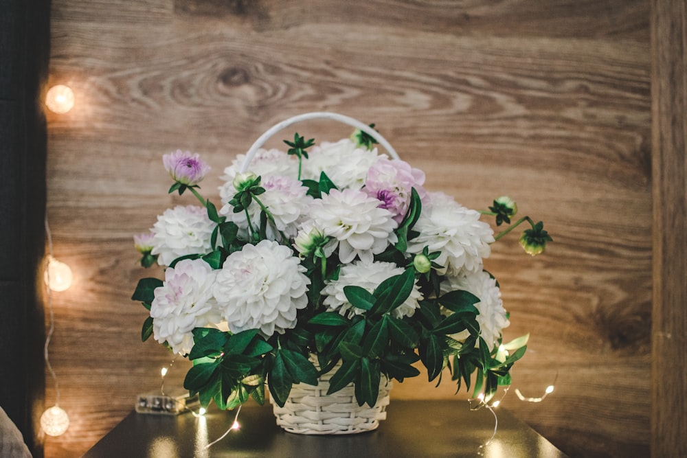 white petaled flowers in wicker basket on table near wall