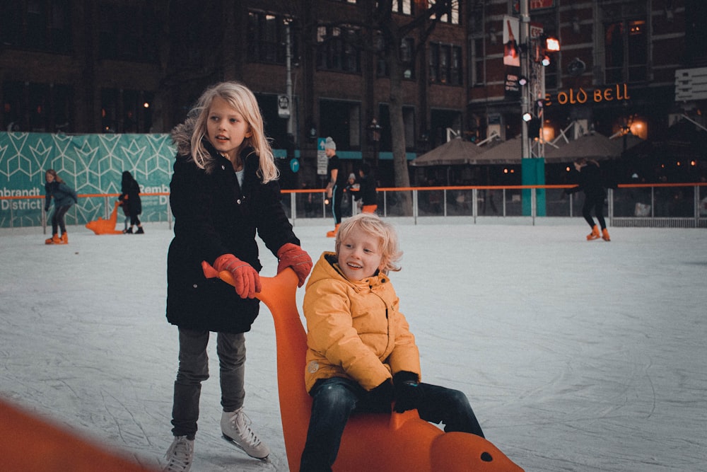 Mädchen schiebt Mädchen reitet auf Spielzeug auf Eisbahn