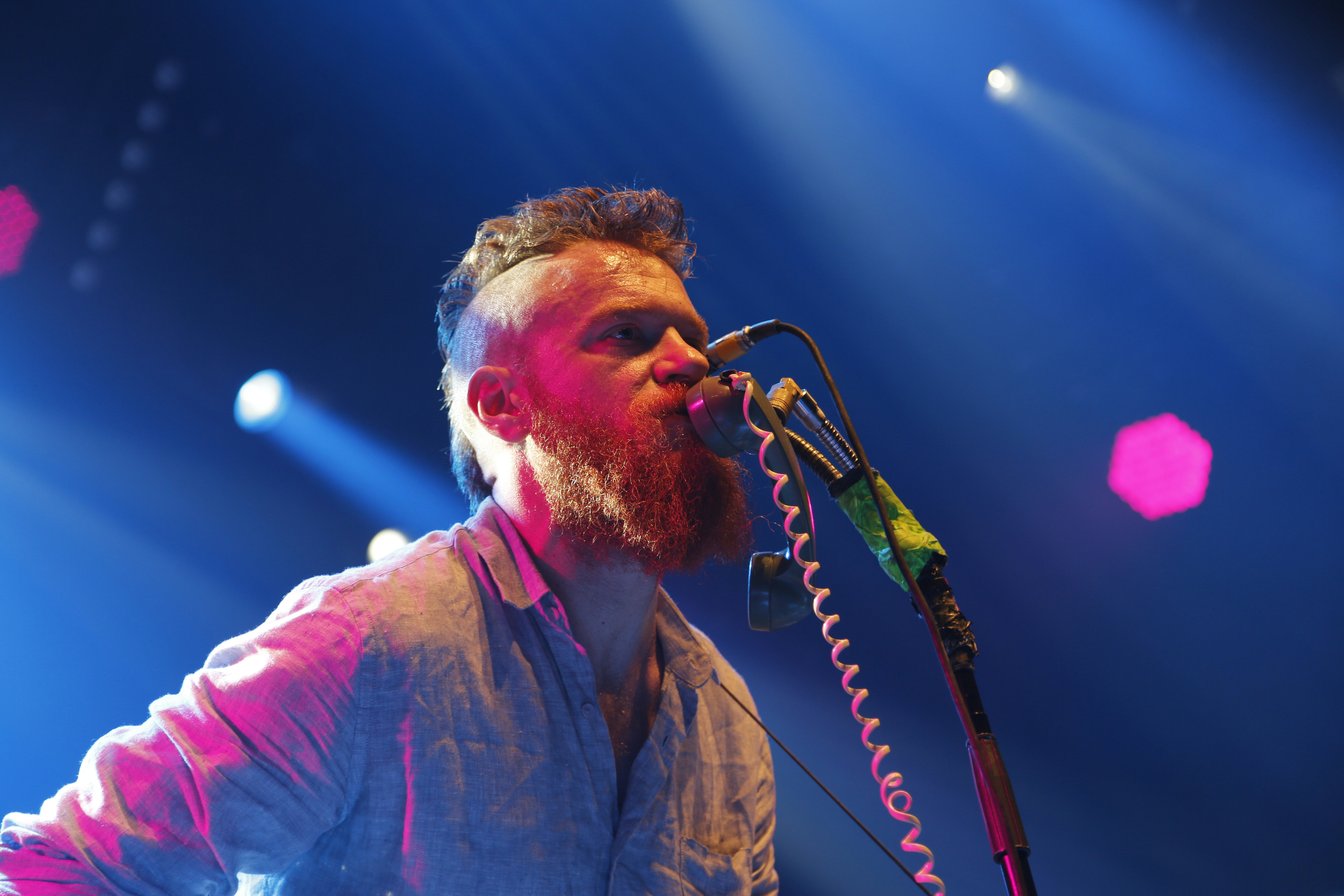 man wearing gray collared button-up long-sleeved shirt singing in front of microphone