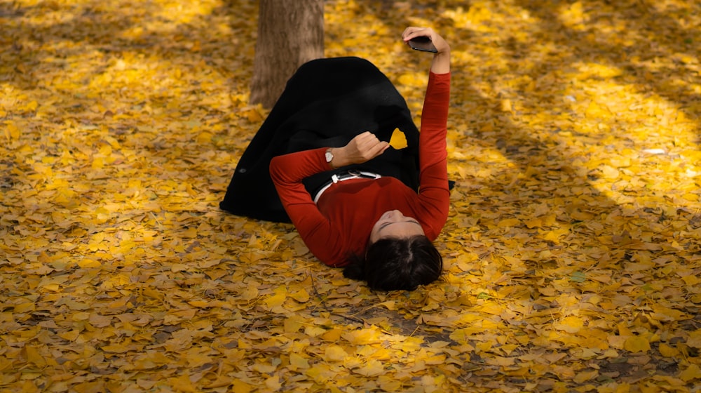 Mujer con blusa roja de manga larga y falda negra acostada sobre hojas secas