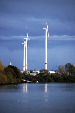 windmills near trees and body of water during day