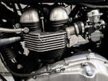 A close-up view of a motorcycle engine, showcasing its metallic components and intricate design. The image highlights elements such as cylinder heads, cooling fins, and various bolts, emphasizing engineering precision.