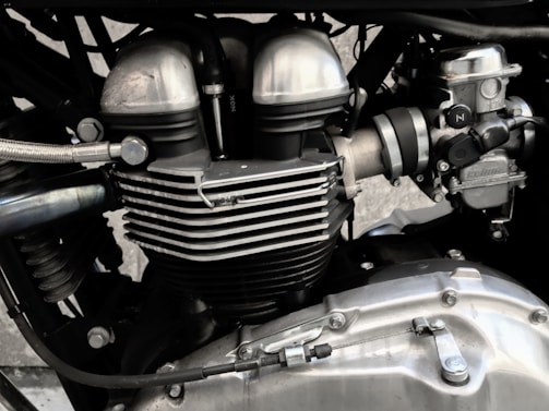 A close-up view of a motorcycle engine, showcasing its metallic components and intricate design. The image highlights elements such as cylinder heads, cooling fins, and various bolts, emphasizing engineering precision.