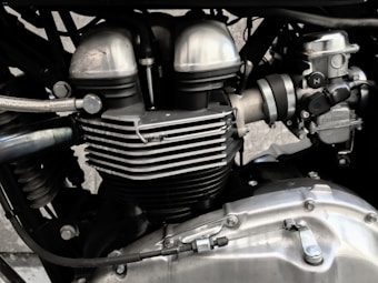 A close-up view of a motorcycle engine, showcasing its metallic components and intricate design. The image highlights elements such as cylinder heads, cooling fins, and various bolts, emphasizing engineering precision.
