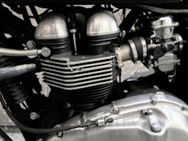 A close-up view of a motorcycle engine, showcasing its metallic components and intricate design. The image highlights elements such as cylinder heads, cooling fins, and various bolts, emphasizing engineering precision.
