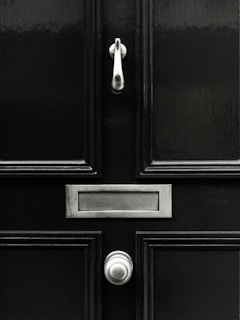 A classic black door with a shiny knocker and clean lines against a brick wall.
