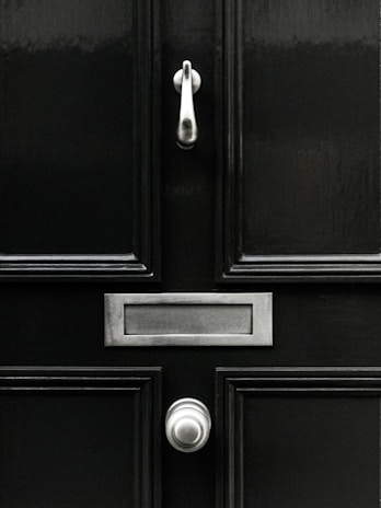 A classic black door with a shiny knocker and clean lines against a brick wall.