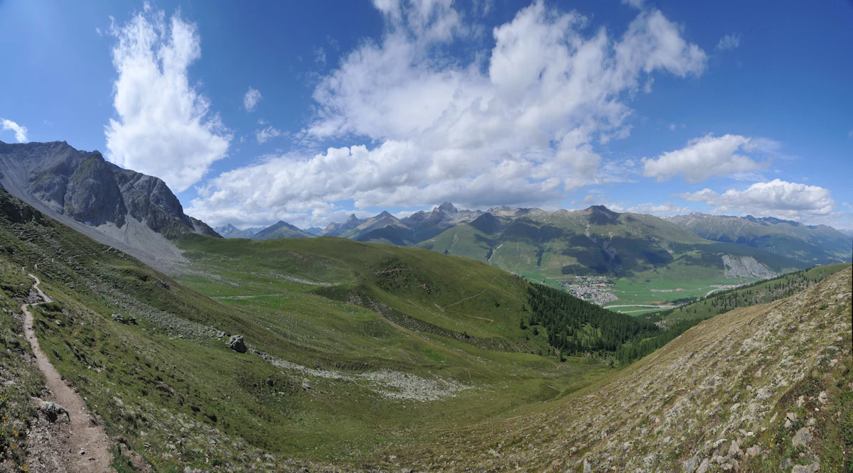 A dirt trail across green alpine pasture at Alp Arpiglia above Zuoz, looking down the Engadin valley