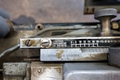 An industrial metal machine component displaying a scale for measuring thickness in points, alongside measurements labeled 'STROKE IN CICEROS'. The device has a metallic knob and visible screws, with some wear and signs of aging on the metallic surface.