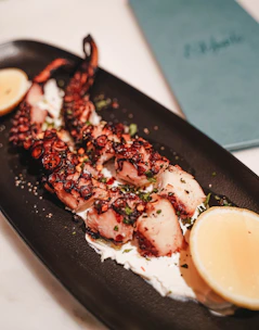 Elegant dish featuring grilled octopus with a rich, dark sauce on a black plate.