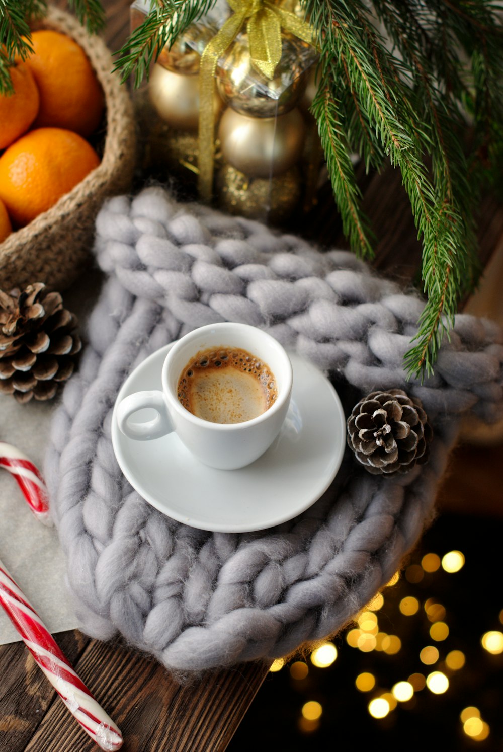 cappuccino on white ceramic mug near brown pinecone, gold baubles, and orange fruits in wicker basket