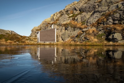 A minimalist retreat cabin made of natural wood and stone, nestled among tall pines and soft beige sand.