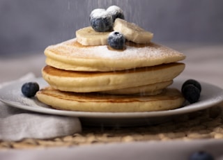three pancakes with blueberries, sliced banana, and sugar on top