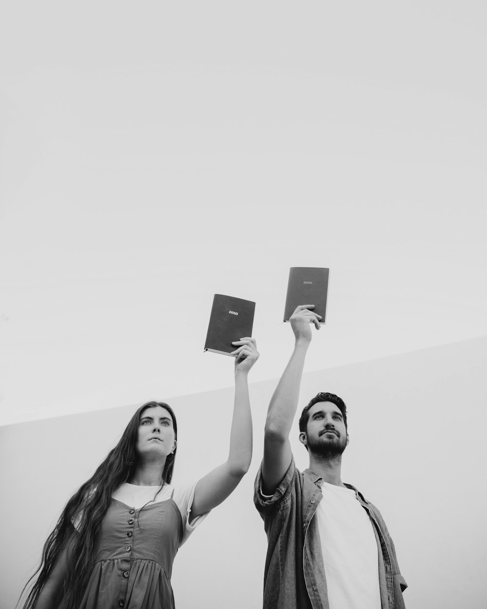 grayscale photography of woman and man holding up books