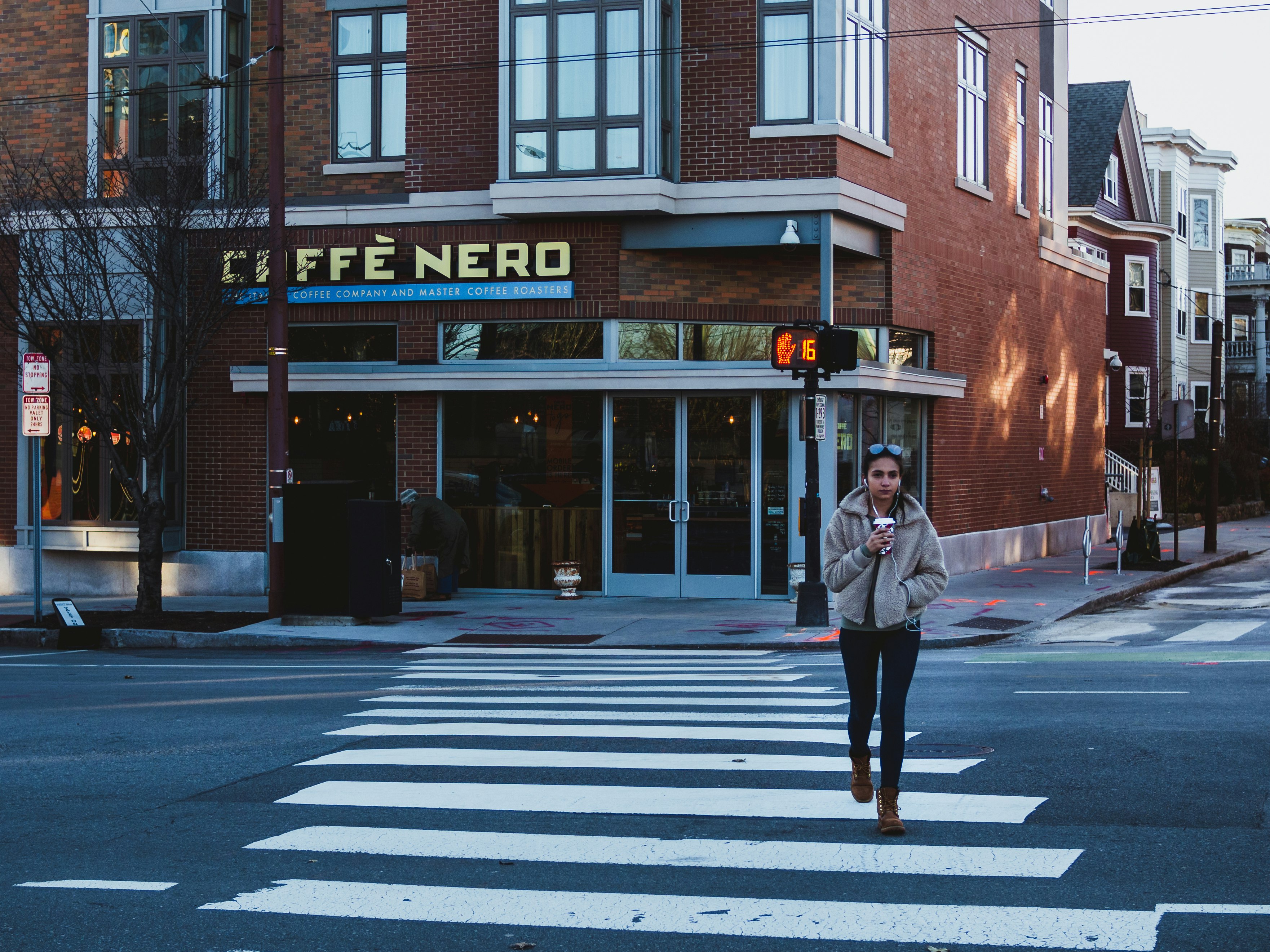 woman wearing gray zip-up jacket crossing on pedestrian lane during daytime