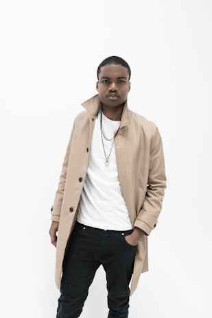 A sleek model wearing a soft beige trench coat paired with minimalist white sneakers, standing against a muted urban backdrop.