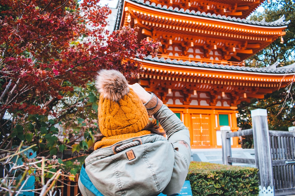 pessoa vestindo jaqueta branca e azul com capuz em pé e de frente perto do santuário xintoísta durante o dia