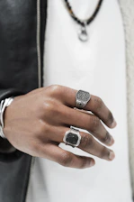 Close-up of a hand wearing layered silver and gold rings against a concrete urban backdrop.