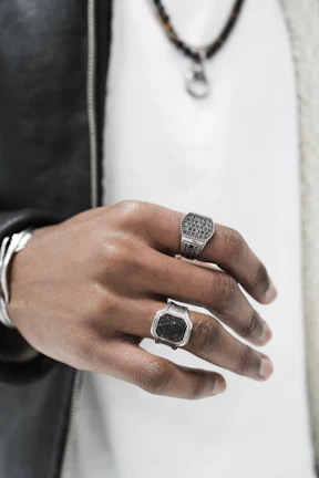 Artistic shot of a hand adorned with bold geometric rings against a muted cityscape backdrop.