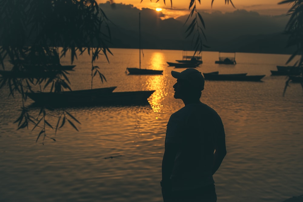 silhouette of person standing near body of water and boats on body of water