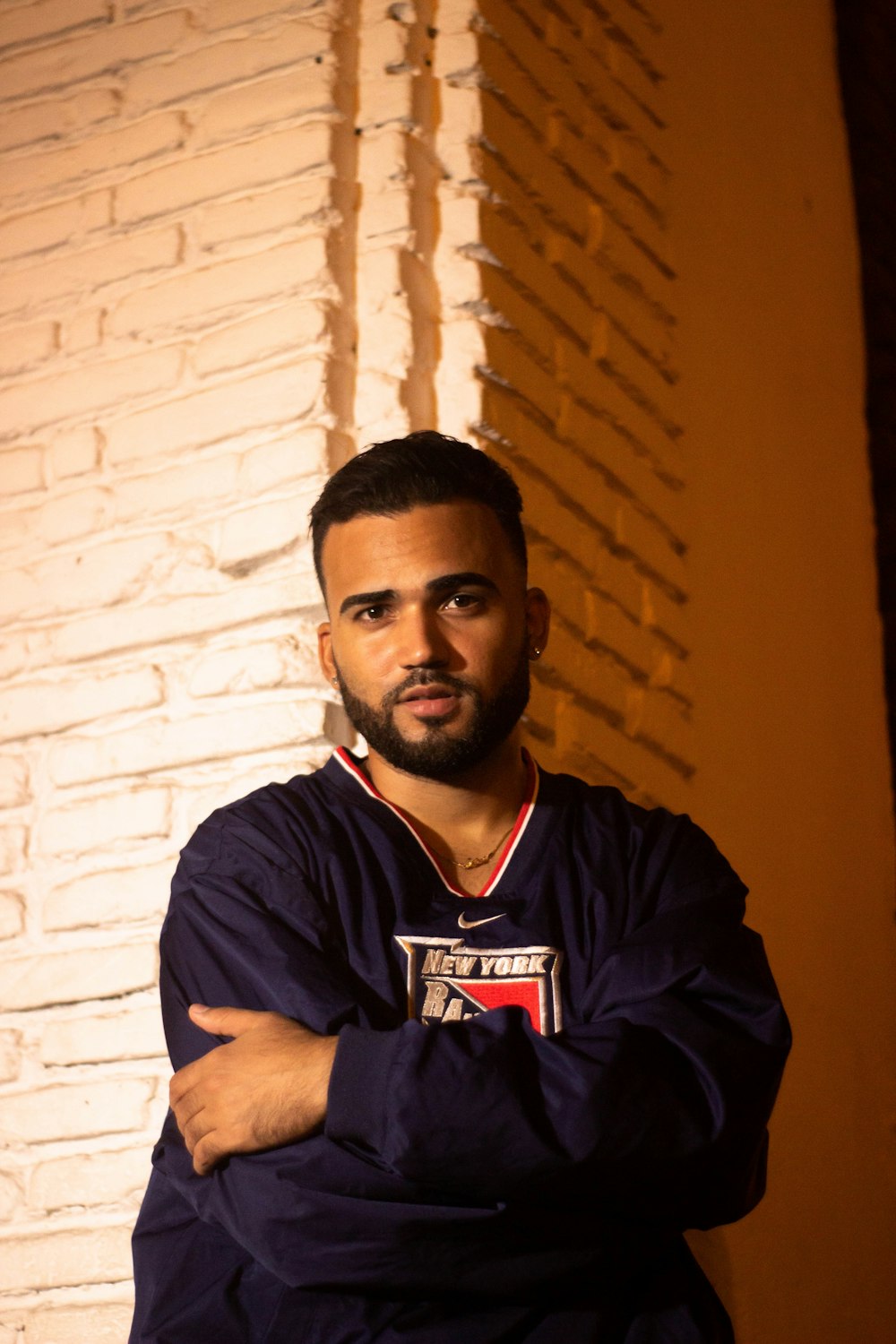 a man with his arms crossed standing in front of a brick wall