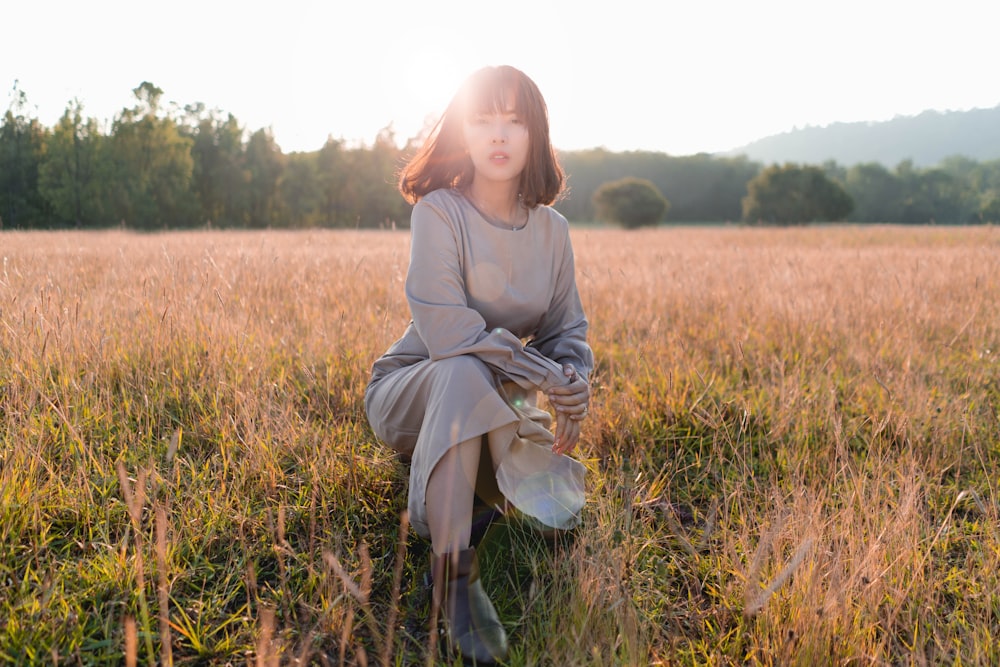 woman sitting on grass field during daytime while wearing gray long-sleeved dress