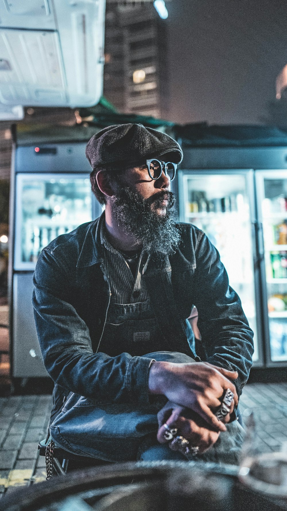 man wearing blue denim jacket and eyeglasses sitting near pavement