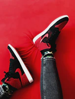 A pair of worn red jeans and sneakers laid out against a rustic wooden backdrop.