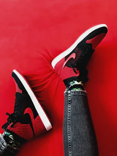 A pair of worn red jeans and sneakers laid out against a rustic wooden backdrop.