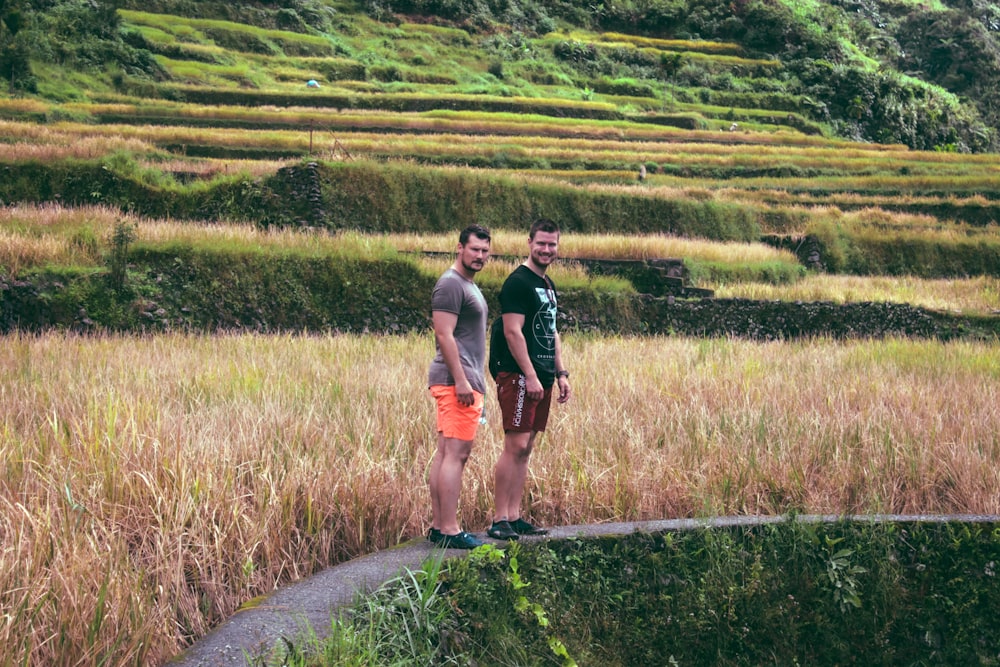 two man standing on pathway near grass and mountain