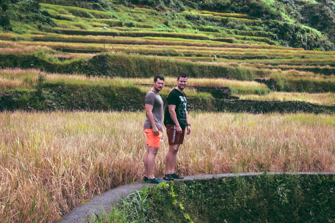 two man standing on pathway near grass and mountain