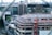 The image depicts a construction site of a large building in an urban area. A partially completed structure with scaffolding covers the upper sections, and workers in safety gear are visible on various levels. Surrounding the site are modern office buildings, some with reflective glass facades. Cranes and other construction equipment are also present in the vicinity.