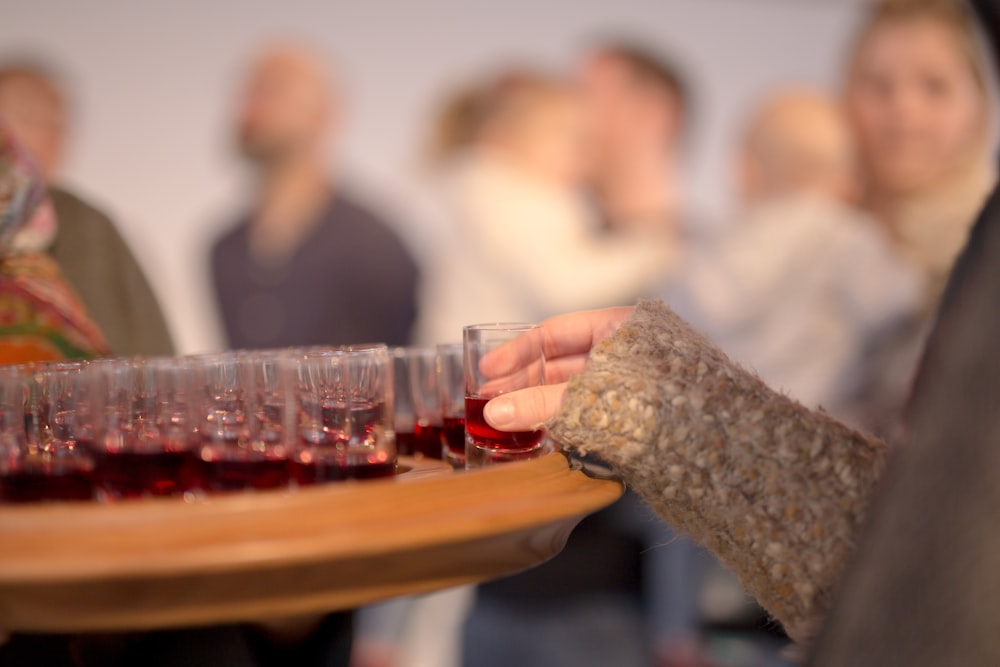 テーブルの上に赤い液体が入ったショットグラスを持っている人
