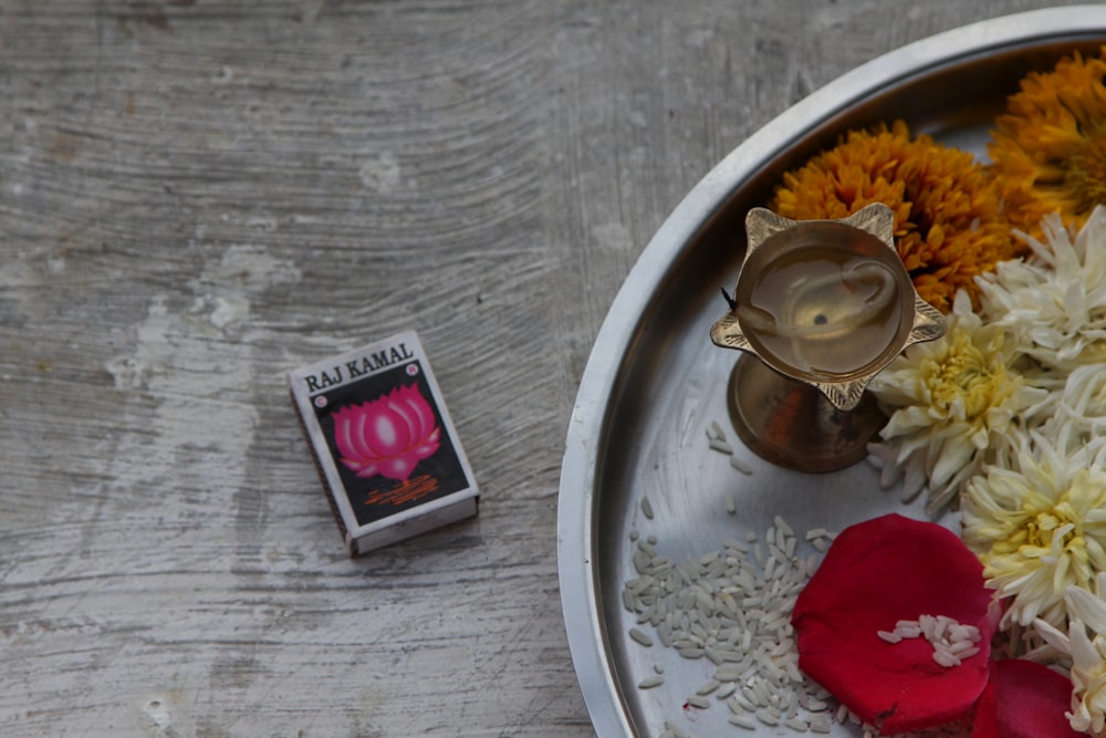 red and white Raj Kamal matchbox beside a tray of flowers and rice grains