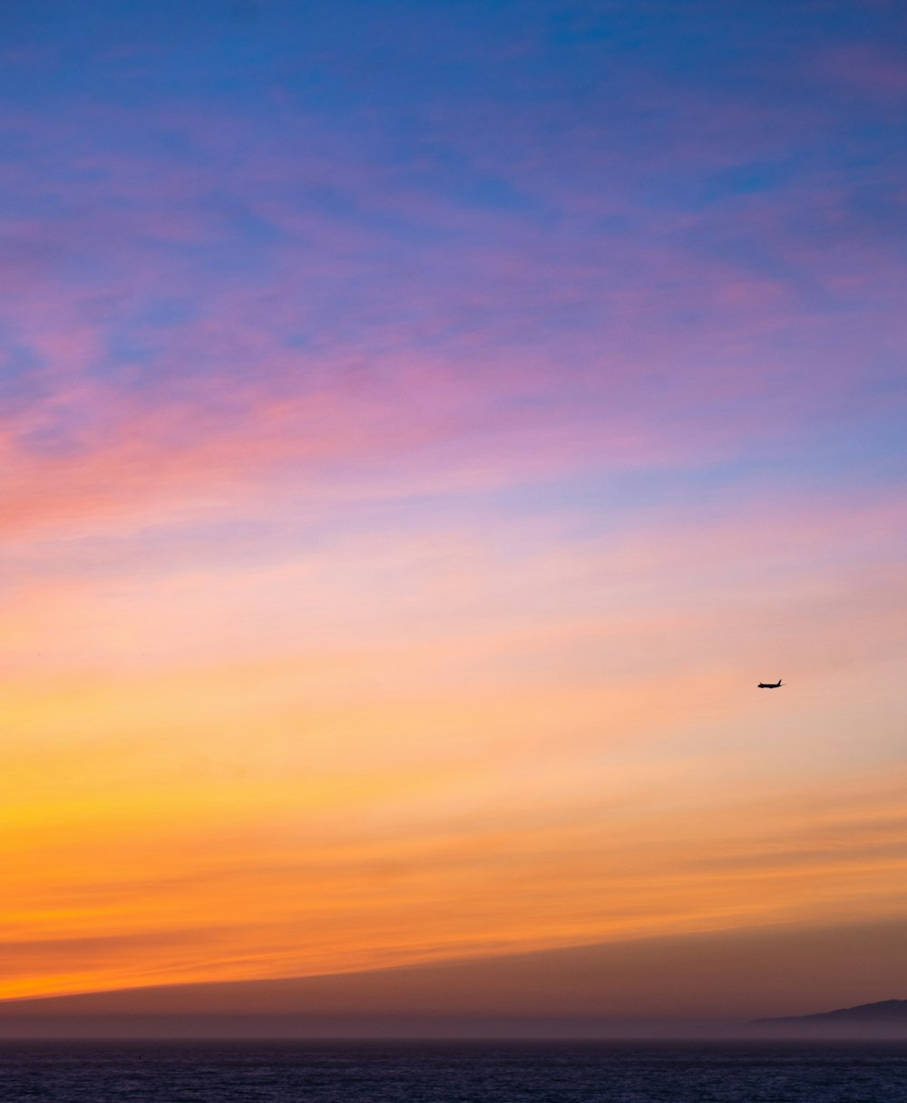 um avião sobrevoando o oceano ao pôr do sol