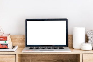 An open laptop on a desk surrounded by books and stationery.