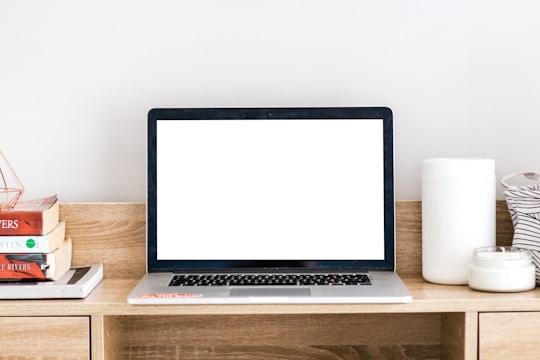 An open laptop on a desk surrounded by books and stationery.